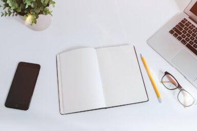 Un livre ouvert sur une table blanche à coté d'un iPhone et d'un MacBook