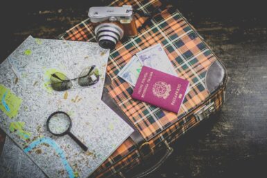 un passeport, une loupe, des lunettes et un appareil photo posés sur un plan et une valise