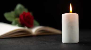 Une bougie blanche à côté d'un livre ouvert avec une rose rouge sur une table noire